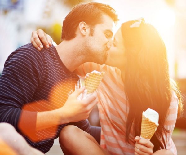 Мужчина и женщина со стаканчиками мороженого в руках целуются