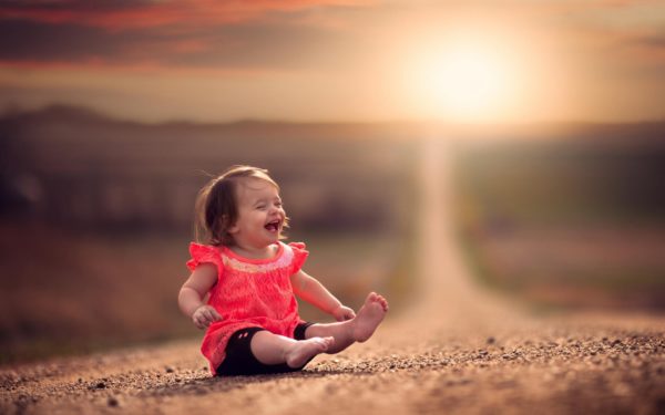 Маленькая девочка сидит на дороге и смеется